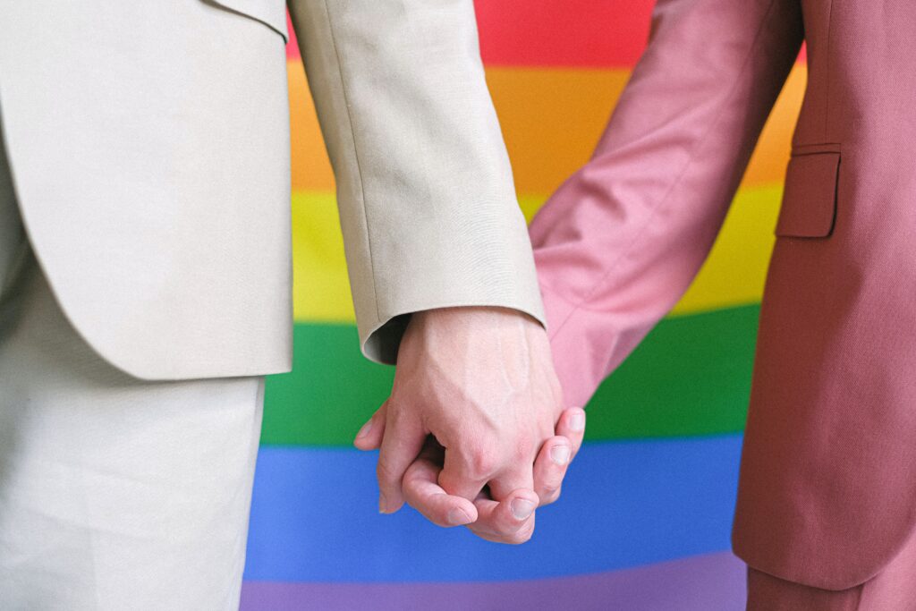 two men holding hands against a Pride flag
