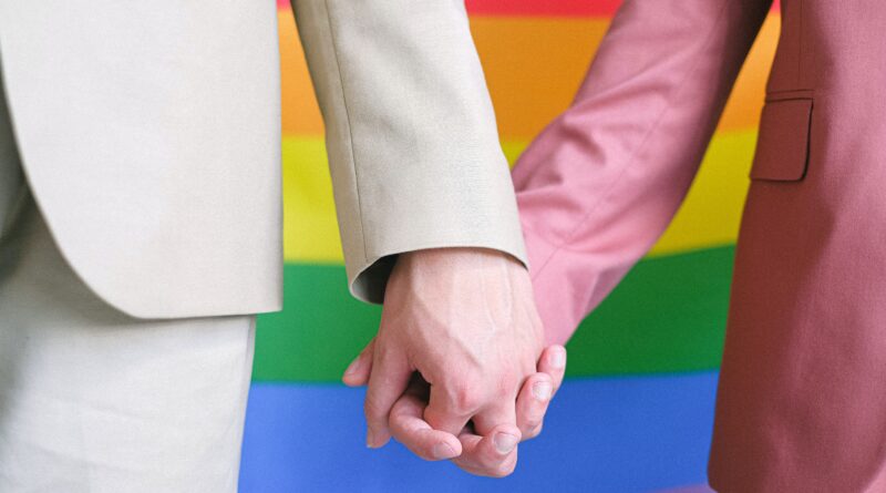two men holding hands against a Pride flag